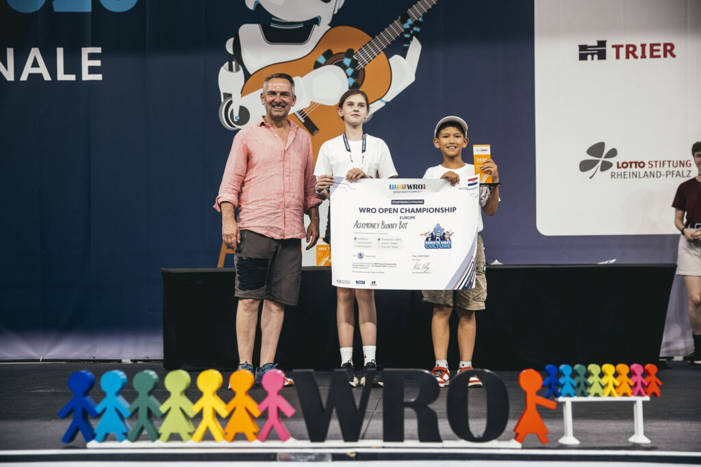 206_2026-06-20_Malte_Hoemberg_WRO_DE_Finale_5707_WEB-1024×683 Zwie Kinder stehen auf einer Bühne und halten einen Scheck in den Händen