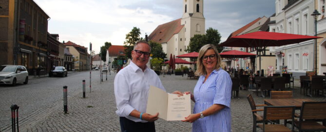 Zwei Menschen stehen mit einer Urkunde auf dem Marktplatz in Lübbenau